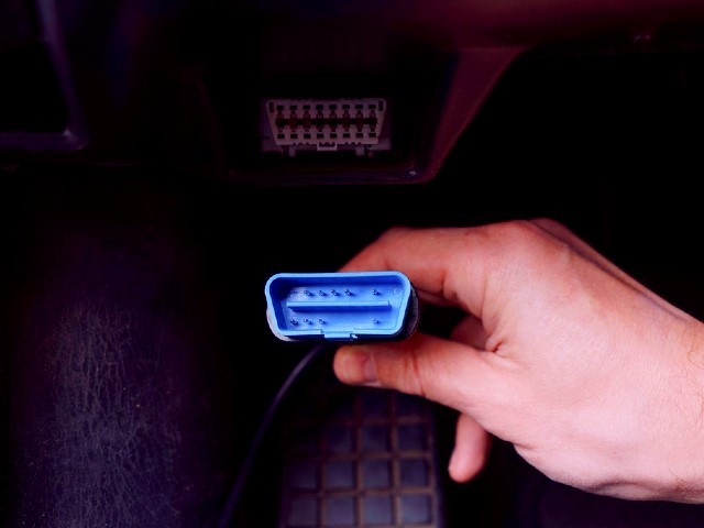 close up of hand holding a blue OBD plug in car for stage chiptuning
